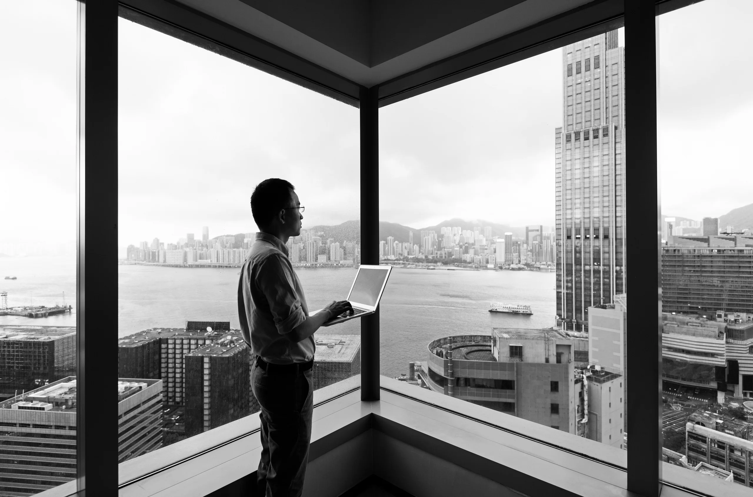 a man standing in front of a window holding a laptop