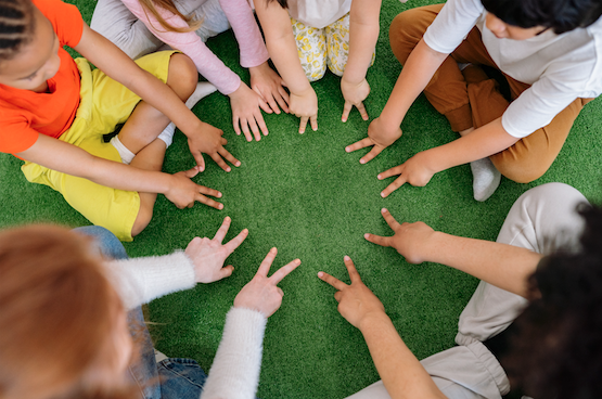 a group of children sitting on the ground holding their hands up