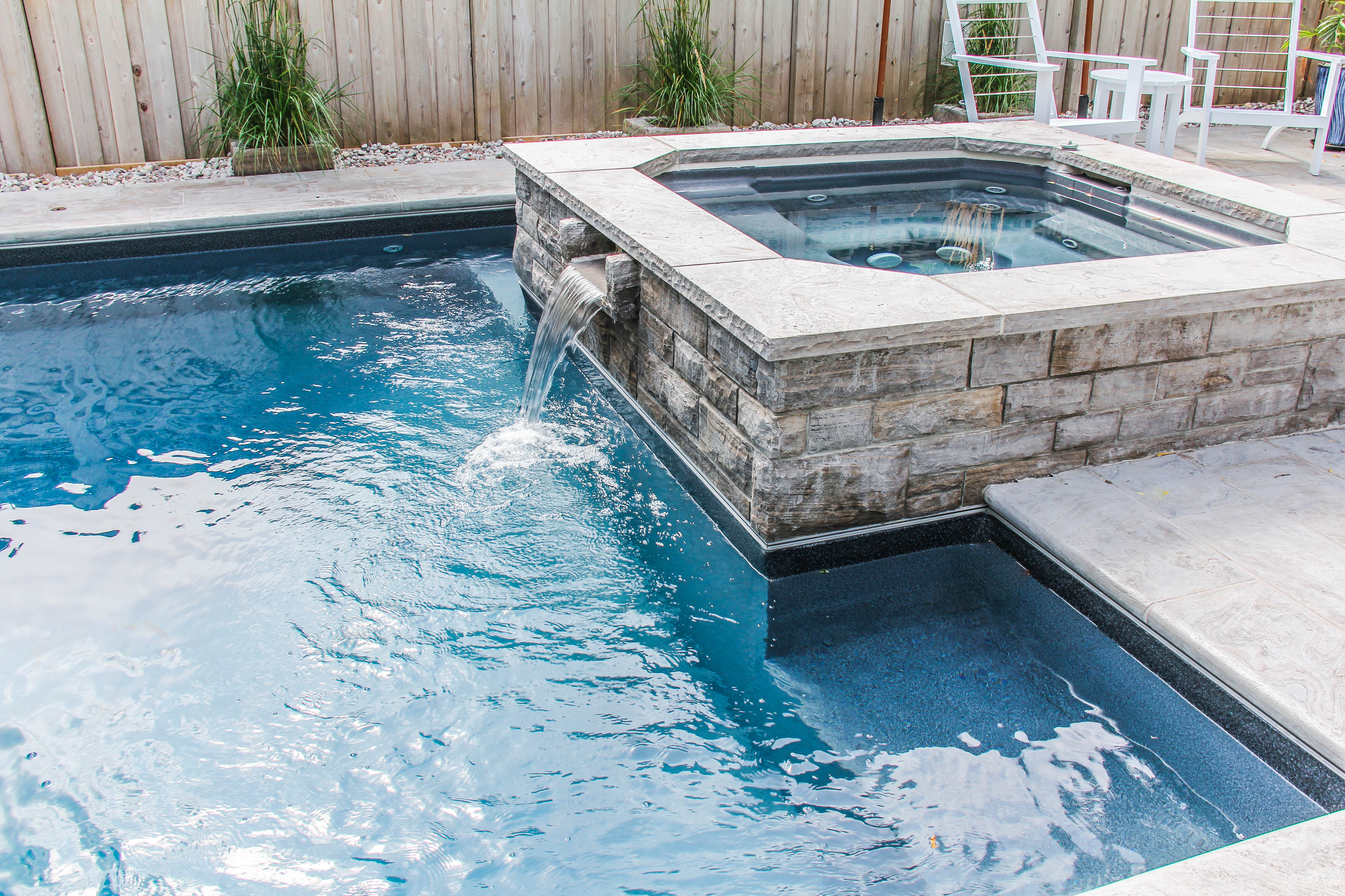 a pool with a hot tub and a stone wall