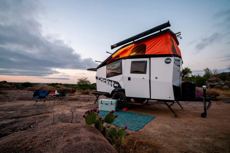 a white and orange camper with a tent on a dirt field