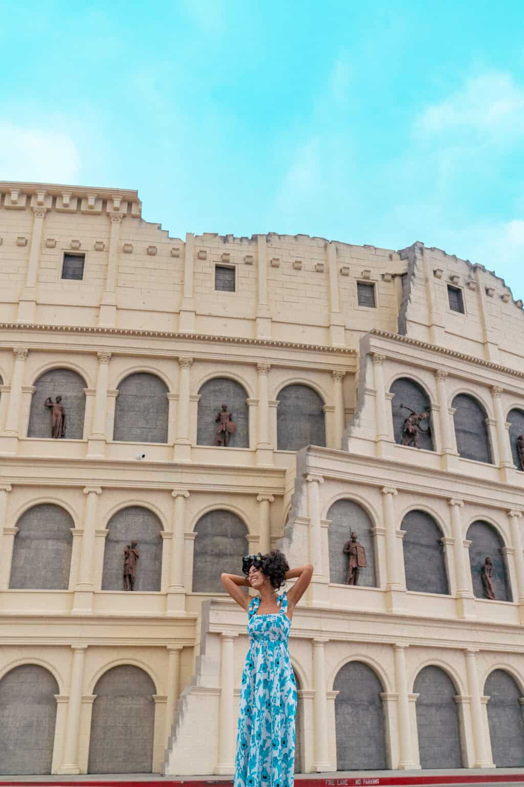 a woman standing in front of a building with a large building with statues