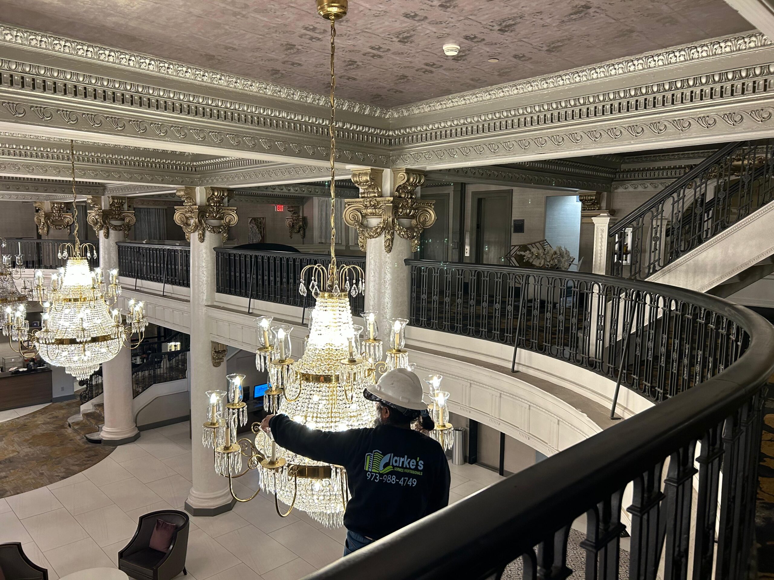 a man in a white helmet and blue shirt standing in a large chandelier