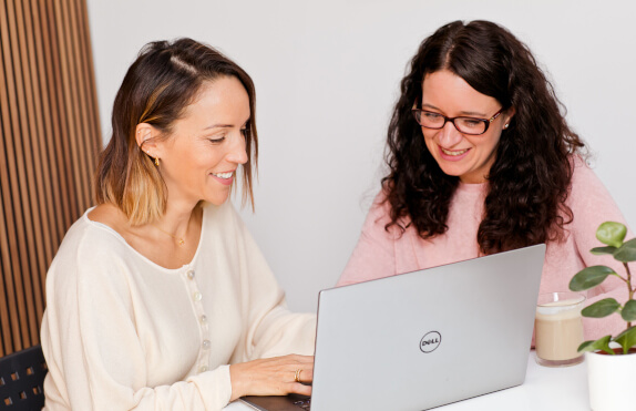 a couple of women looking at a laptop
