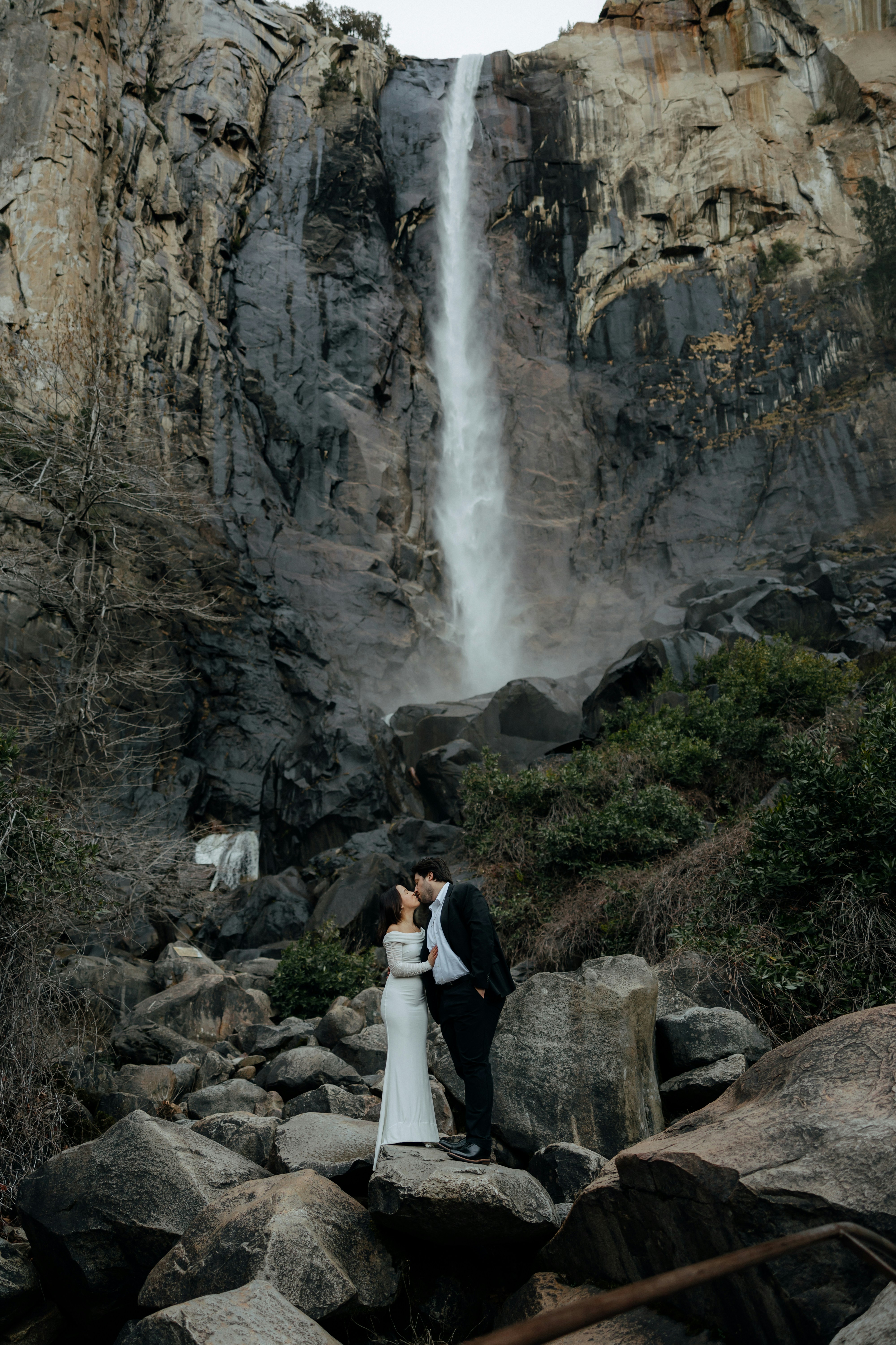 a man and woman kissing in front of a waterfall