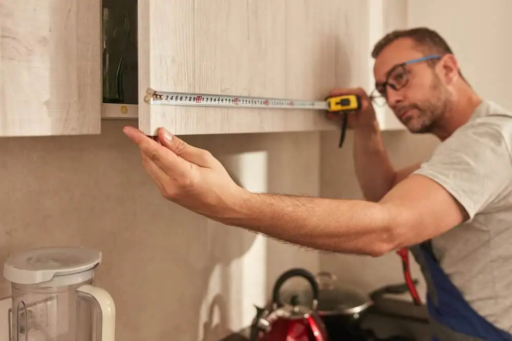 a man measuring a cabinet