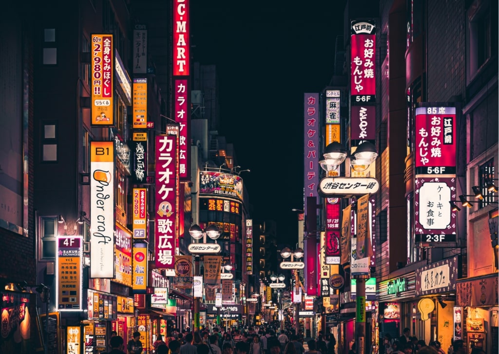 a street with many signs and people walking with Kabukichō, Tokyo in the background