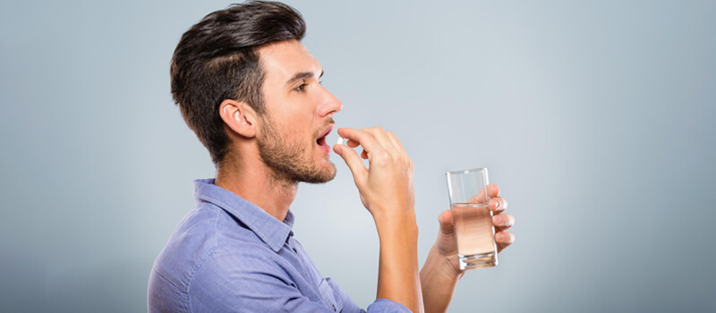 a man taking a pill and holding a glass of water