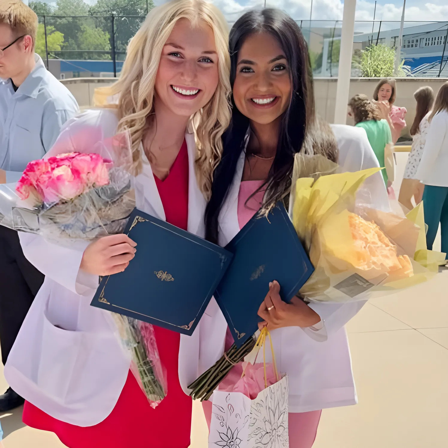 two women holding flowers and diplomas