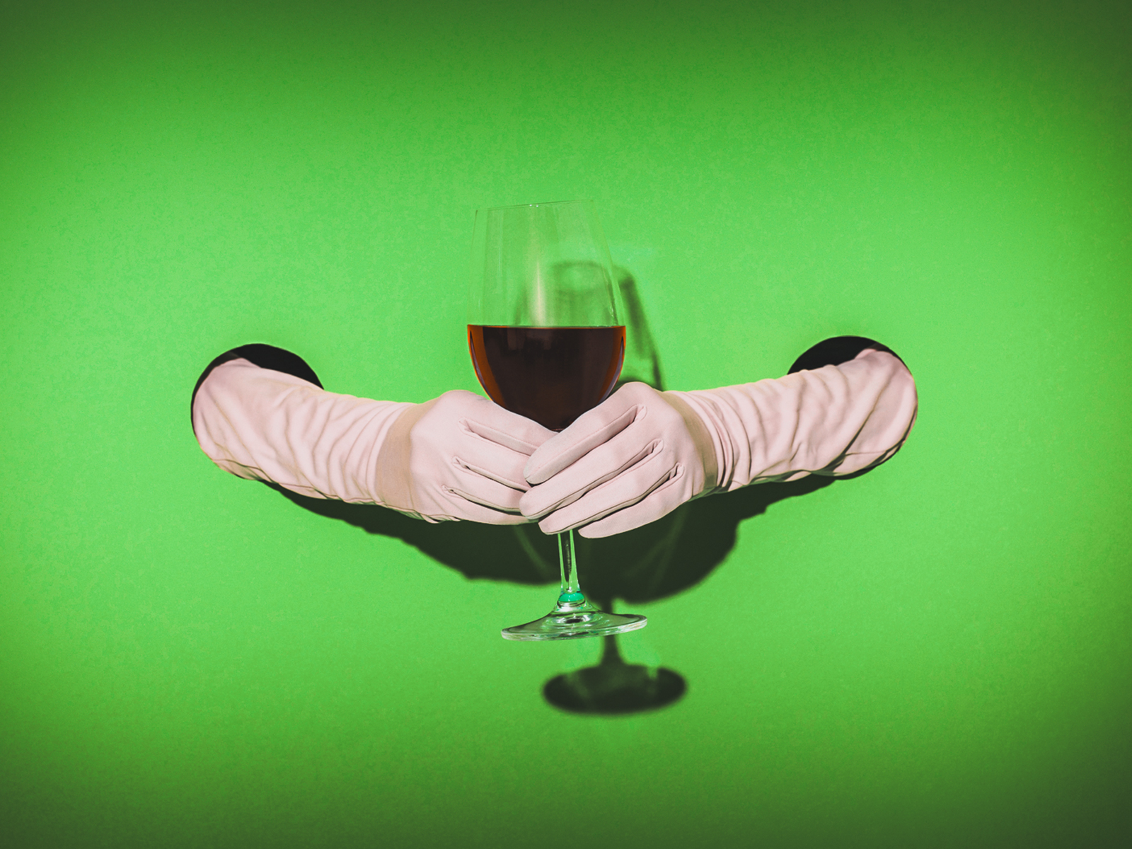 a hand holding a glass of wine through a hole in a wall