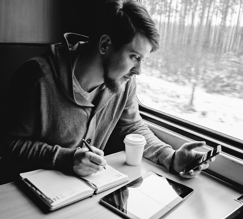 a man sitting at a table writing on a notebook and a phone