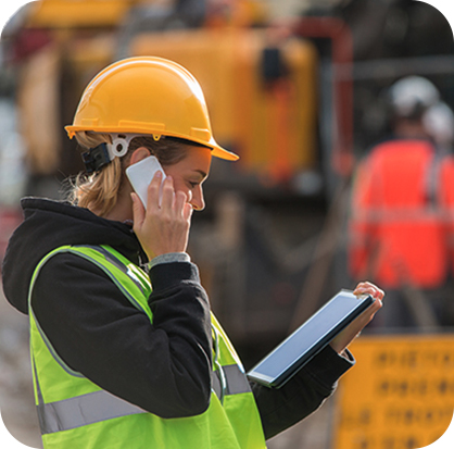 a woman in a yellow hard hat talking on the phone and holding a tablet