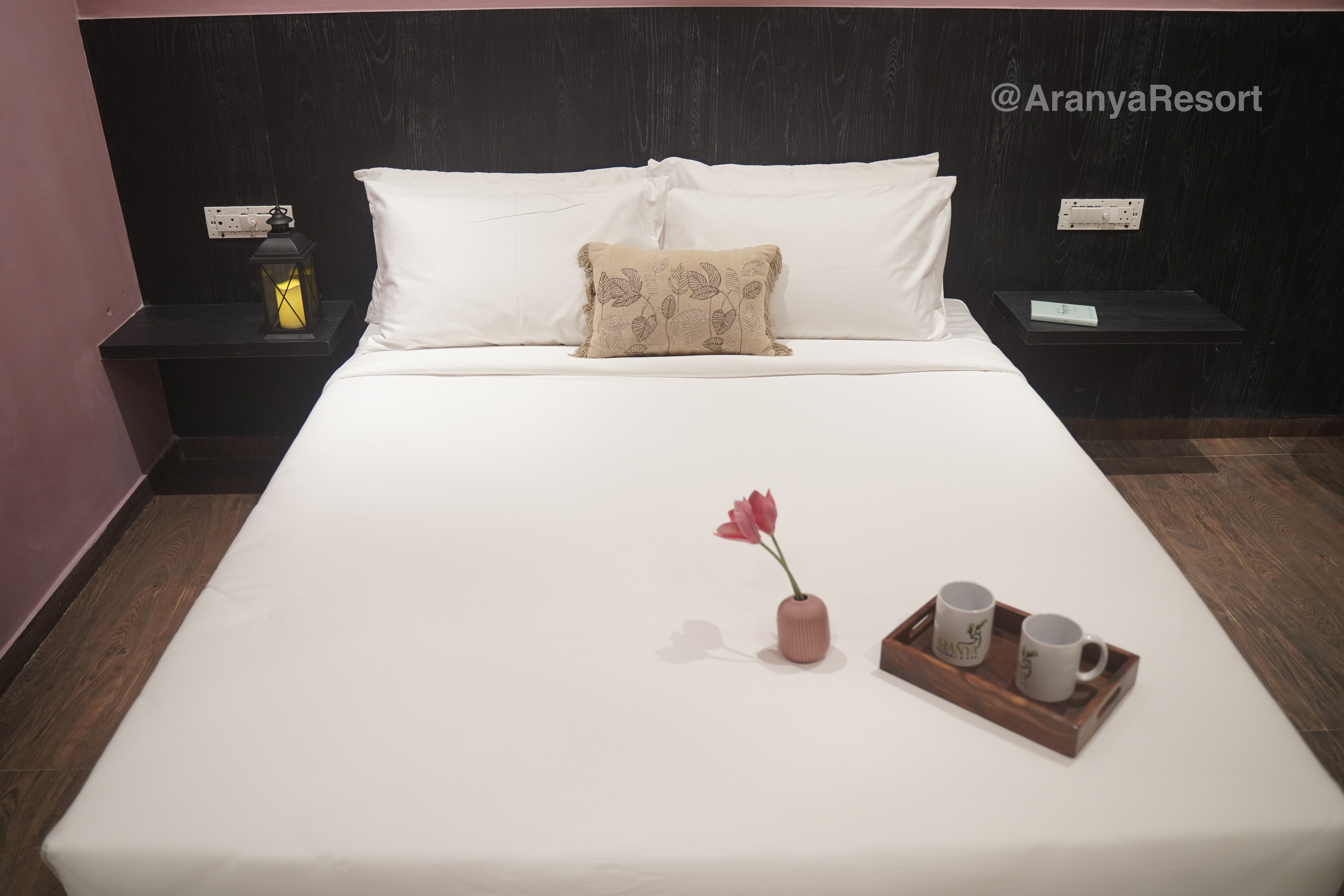 a bed with a tray of coffee cups and a flower on it