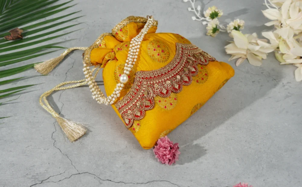 a yellow bag with a gold lace and a pearl necklace