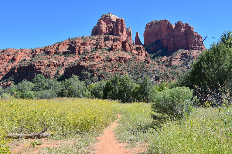 a dirt path through a grassy field with tall red rocks