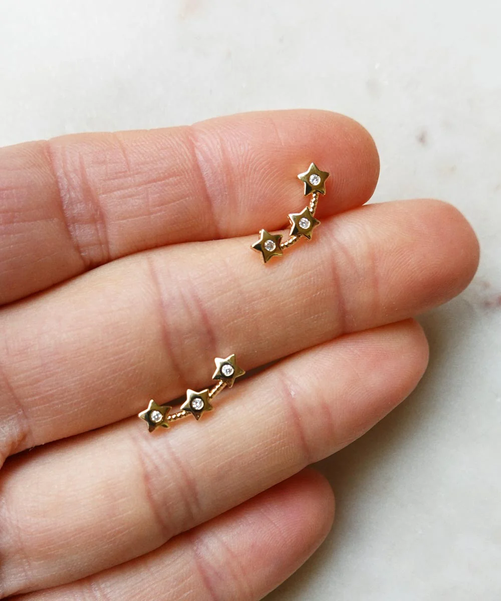 a hand holding two gold stars earrings