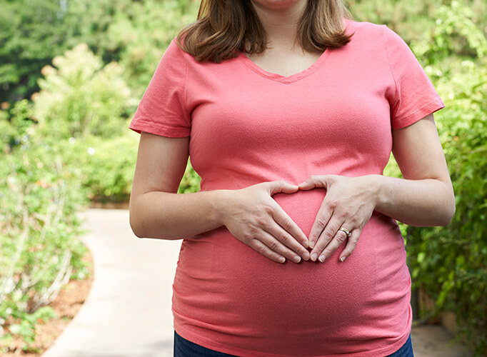 a pregnant woman making a heart with her hands on her belly