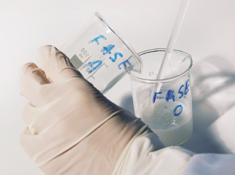 a hand in a glove holding a beaker with a straw