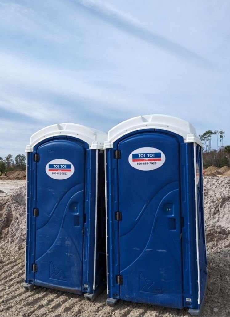 two blue portable toilets in a dirt area