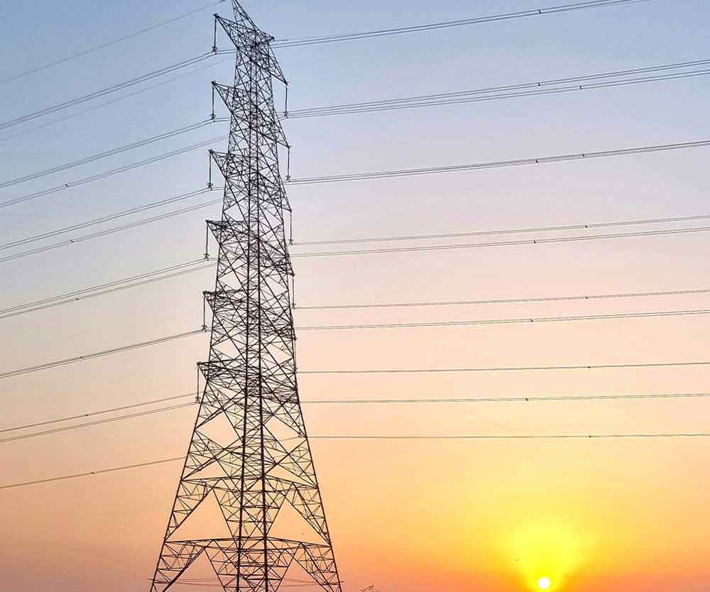 a power line tower with the sun setting behind it