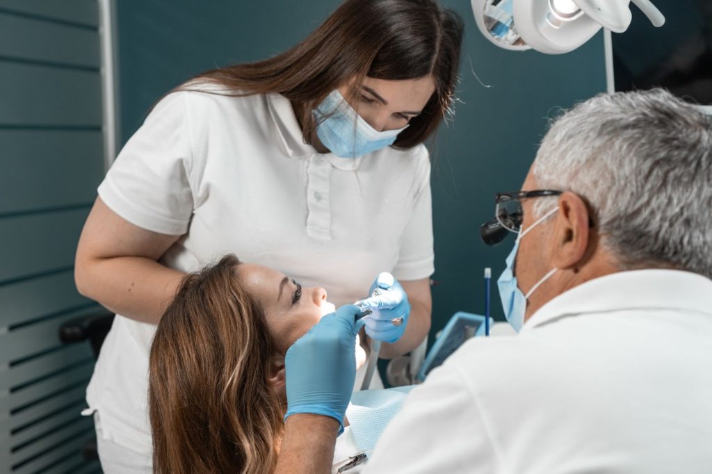 a woman in a white shirt and blue gloves getting her teeth checked