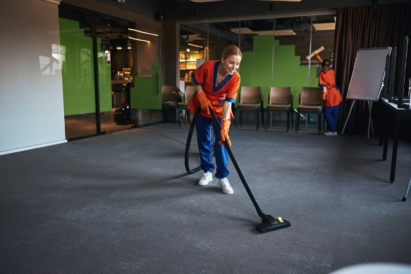 a woman in orange and blue uniform vacuuming the floor