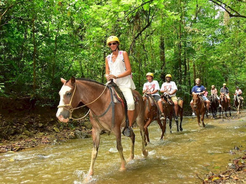 a group of people riding horses through a stream