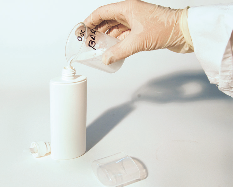 a hand pouring liquid into a plastic container