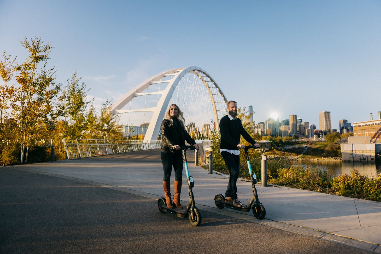 a man and woman riding scooters on a bridge
