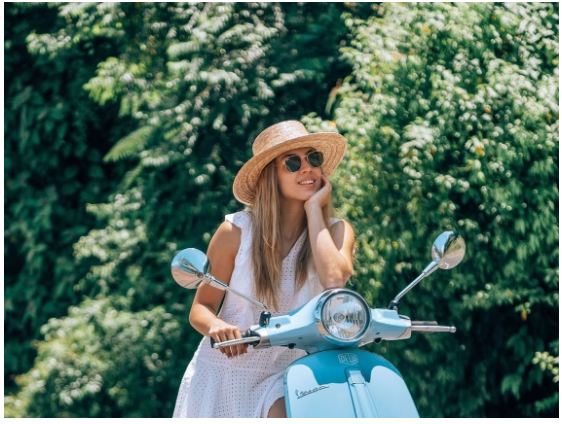 a woman wearing a hat and sunglasses sitting on a blue scooter