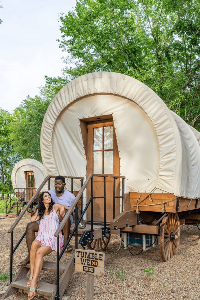 a man and woman sitting on stairs in front of a covered wagon