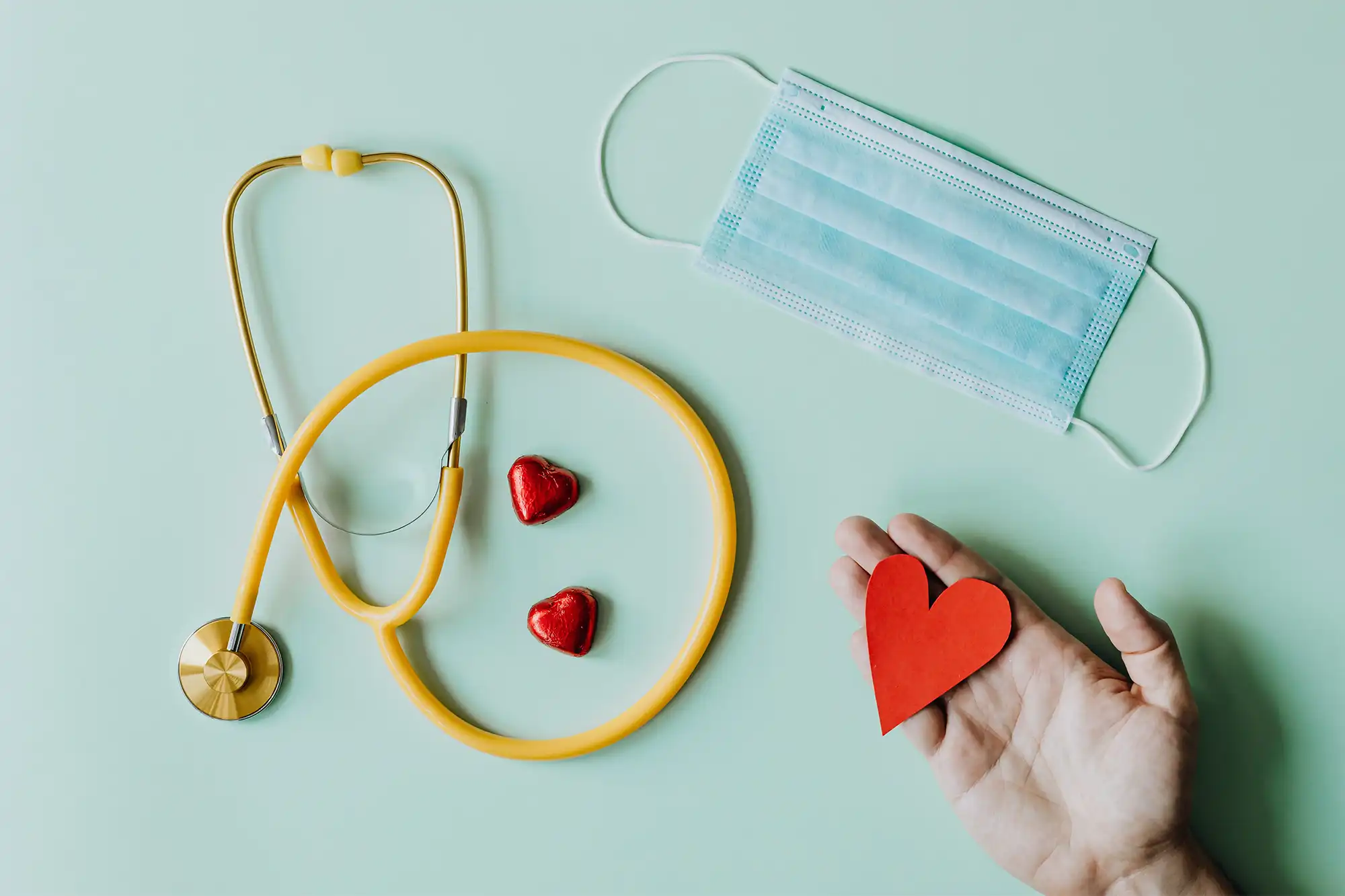 a hand holding a heart next to a stethoscope and a mask