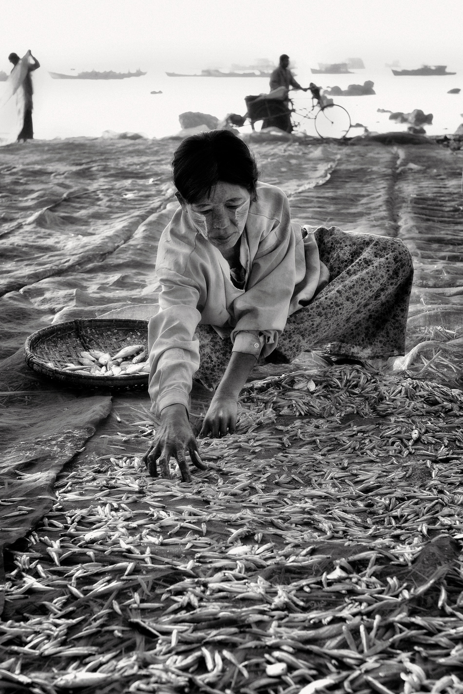 a woman sitting on the ground with a basket full of fish