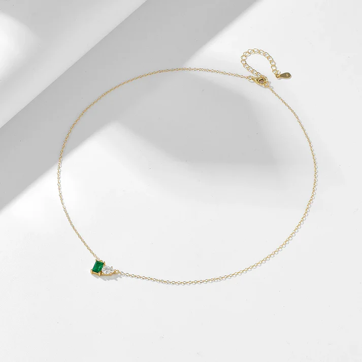 a gold chain with a green stone and a small square gem on it