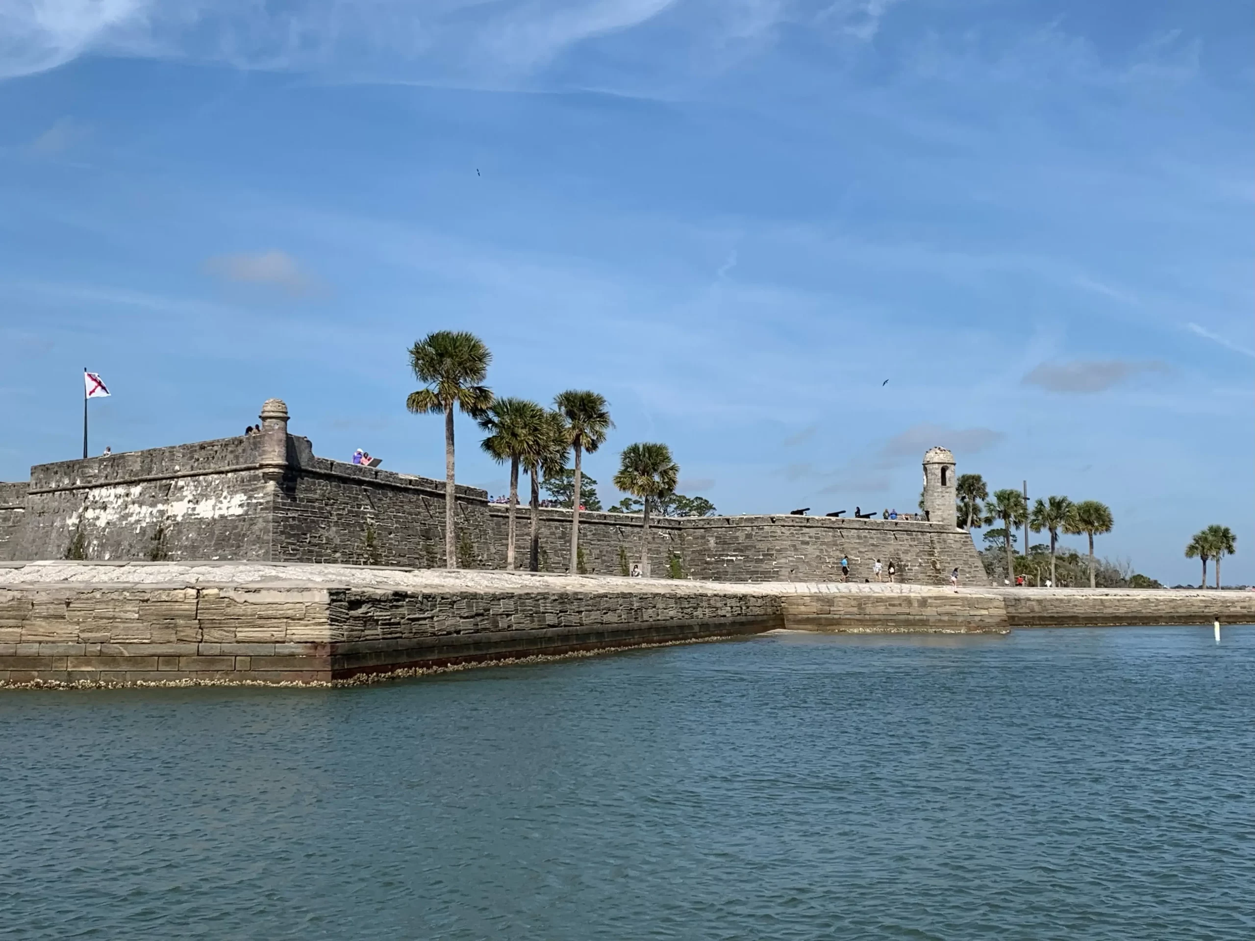 a stone wall with palm trees and a body of water