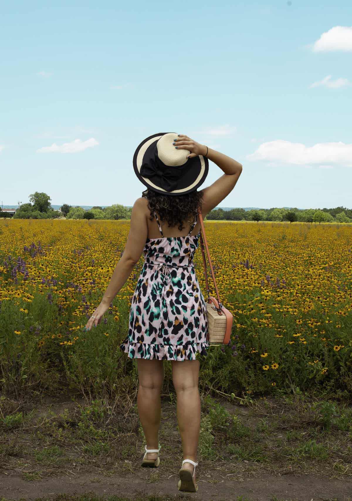a woman in a dress and hat standing in a field of flowers