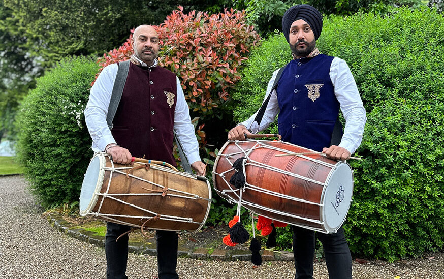 two men holding drums in front of bushes