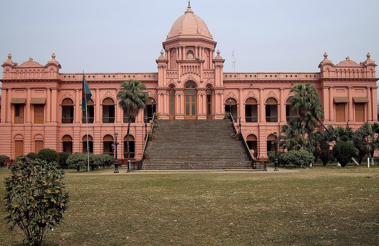a pink building with a large staircase with Ahsan Manzil in the background