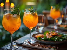 a group of glasses of orange liquid with ice and mint leaves on a table