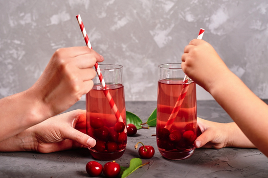 a pair of hands holding straws to a glass of red liquid