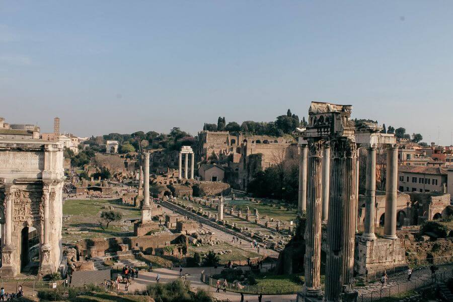 a group of people walking around a ruins with Roman Forum in the background