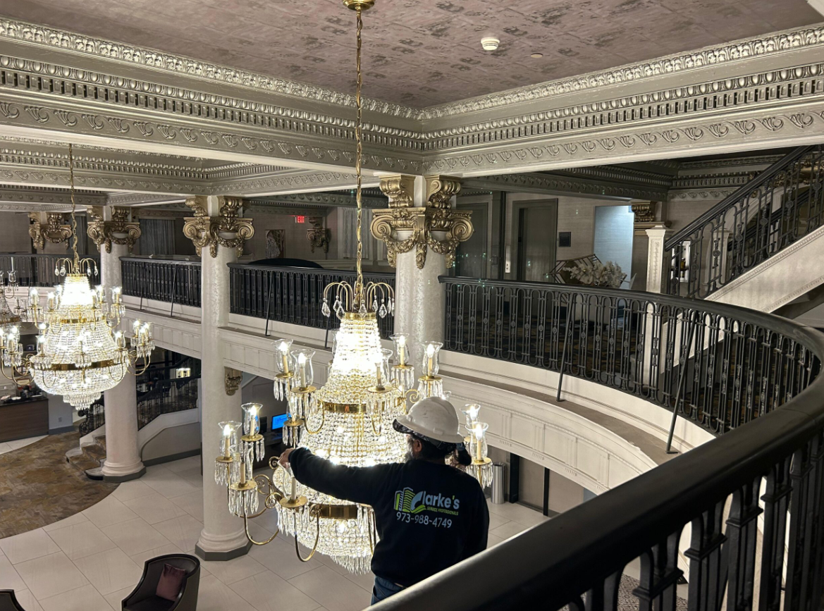 a man in a white hat and blue shirt installing a chandelier