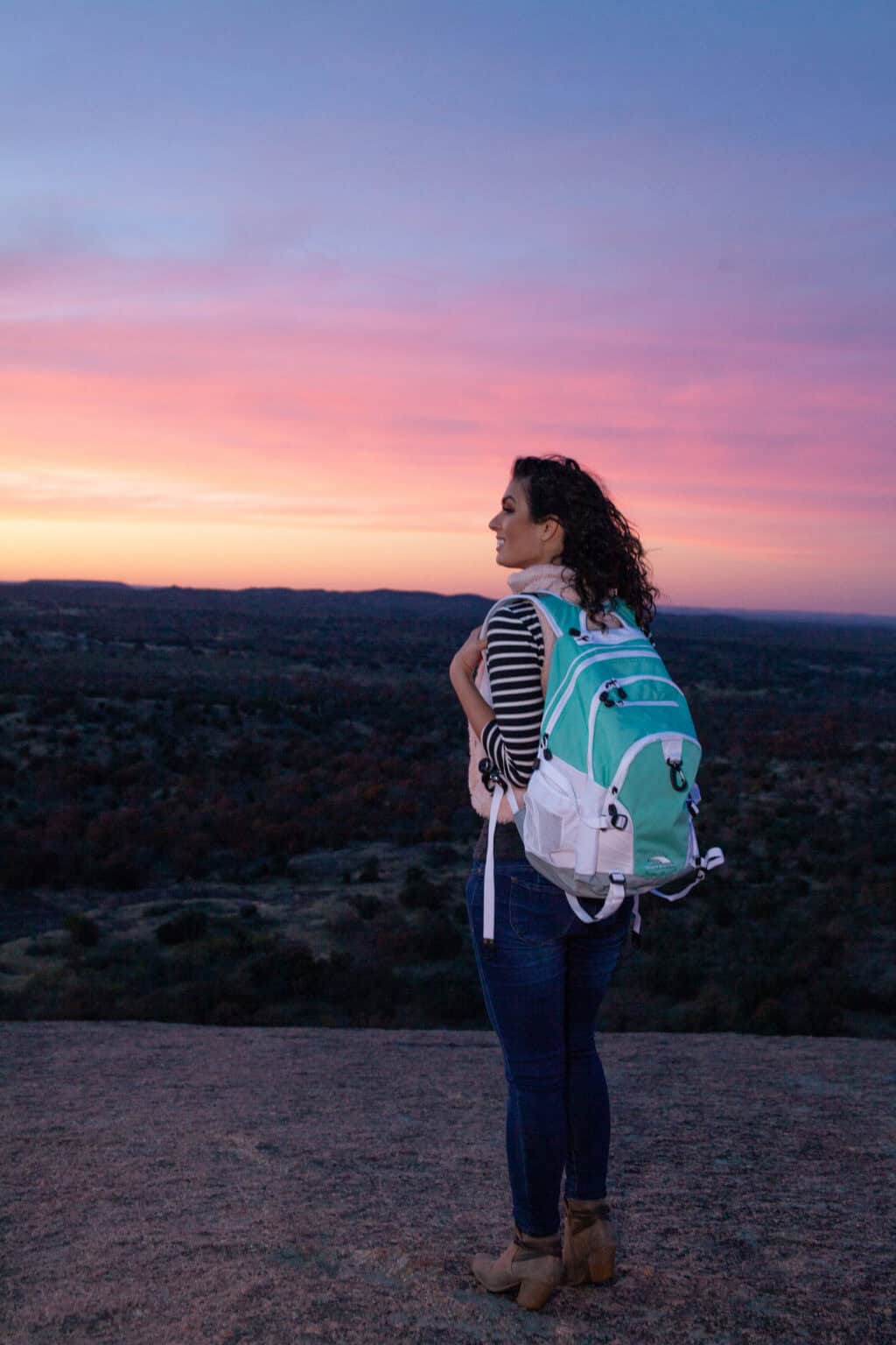 a woman with a backpack looking at a sunset