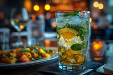 a glass of water with ice and orange slices on a plate of food