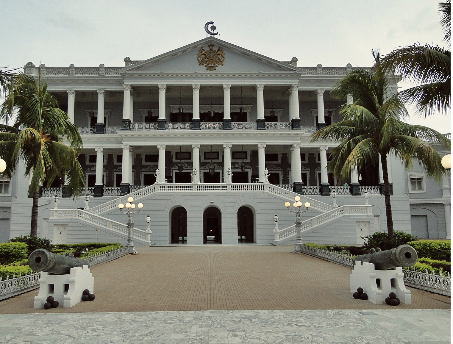 a large white building with columns and a walkway with Falaknuma Palace in the background