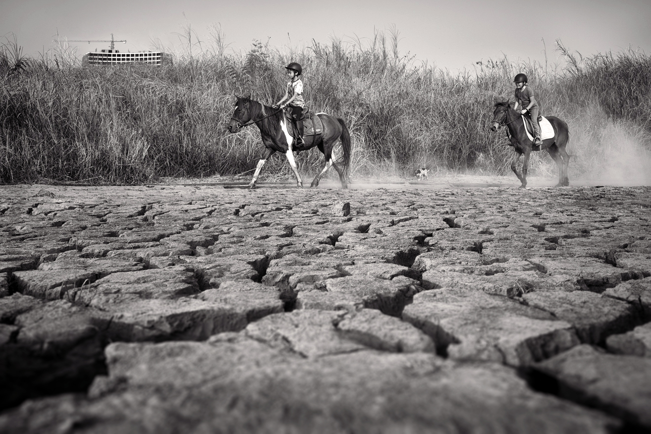 a couple of people riding horses on a dry cracked ground