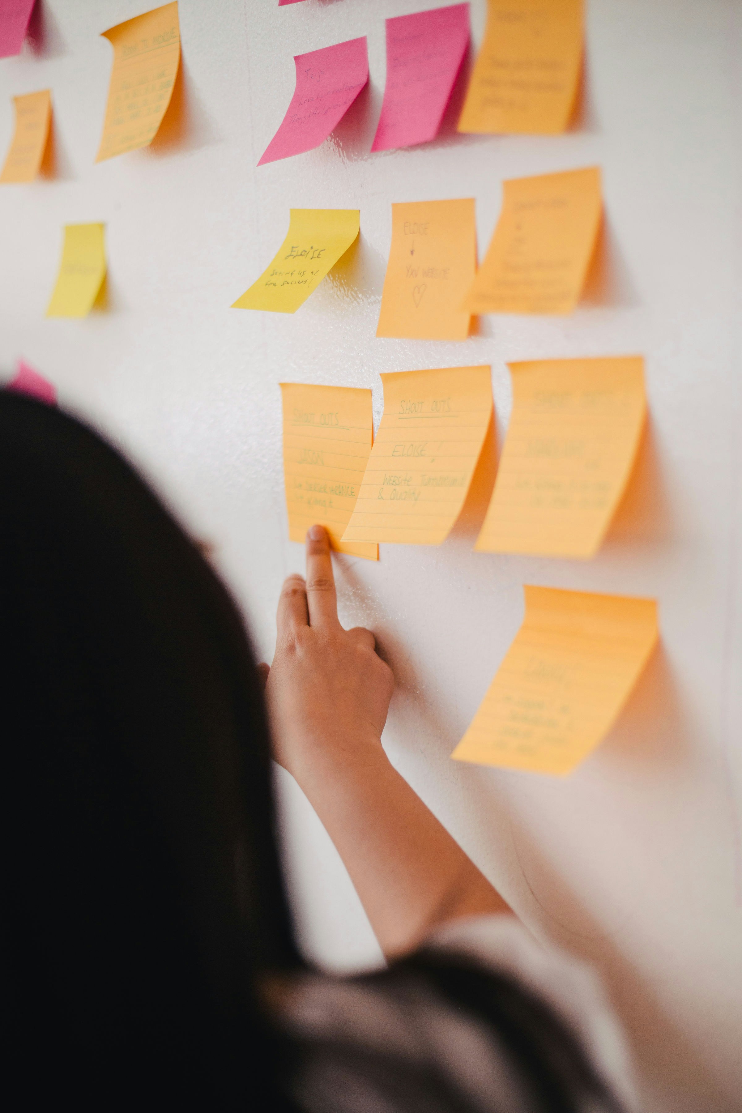 a person pointing at a wall with yellow sticky notes