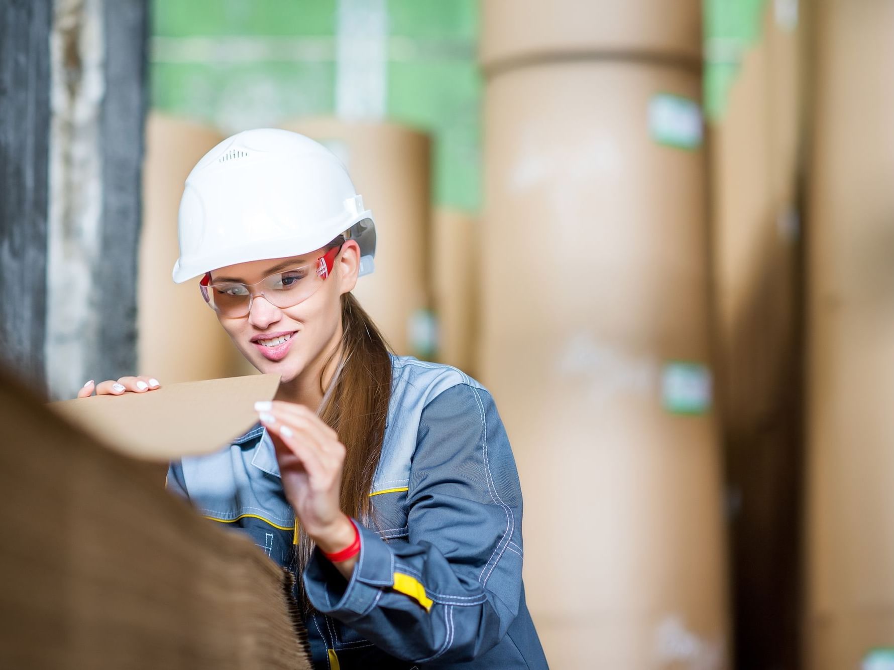 a woman wearing a hard hat and glasses looking at a piece of cardboard
