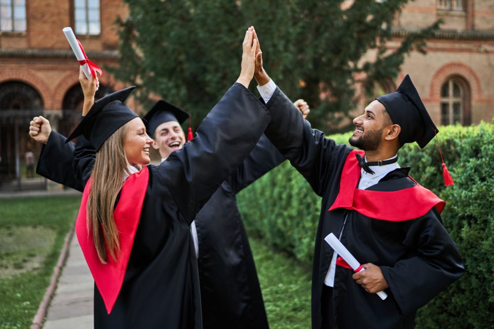 a group of people in graduation gowns and caps giving each other a high five