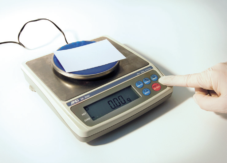 a person's finger pressing a paper on a scale