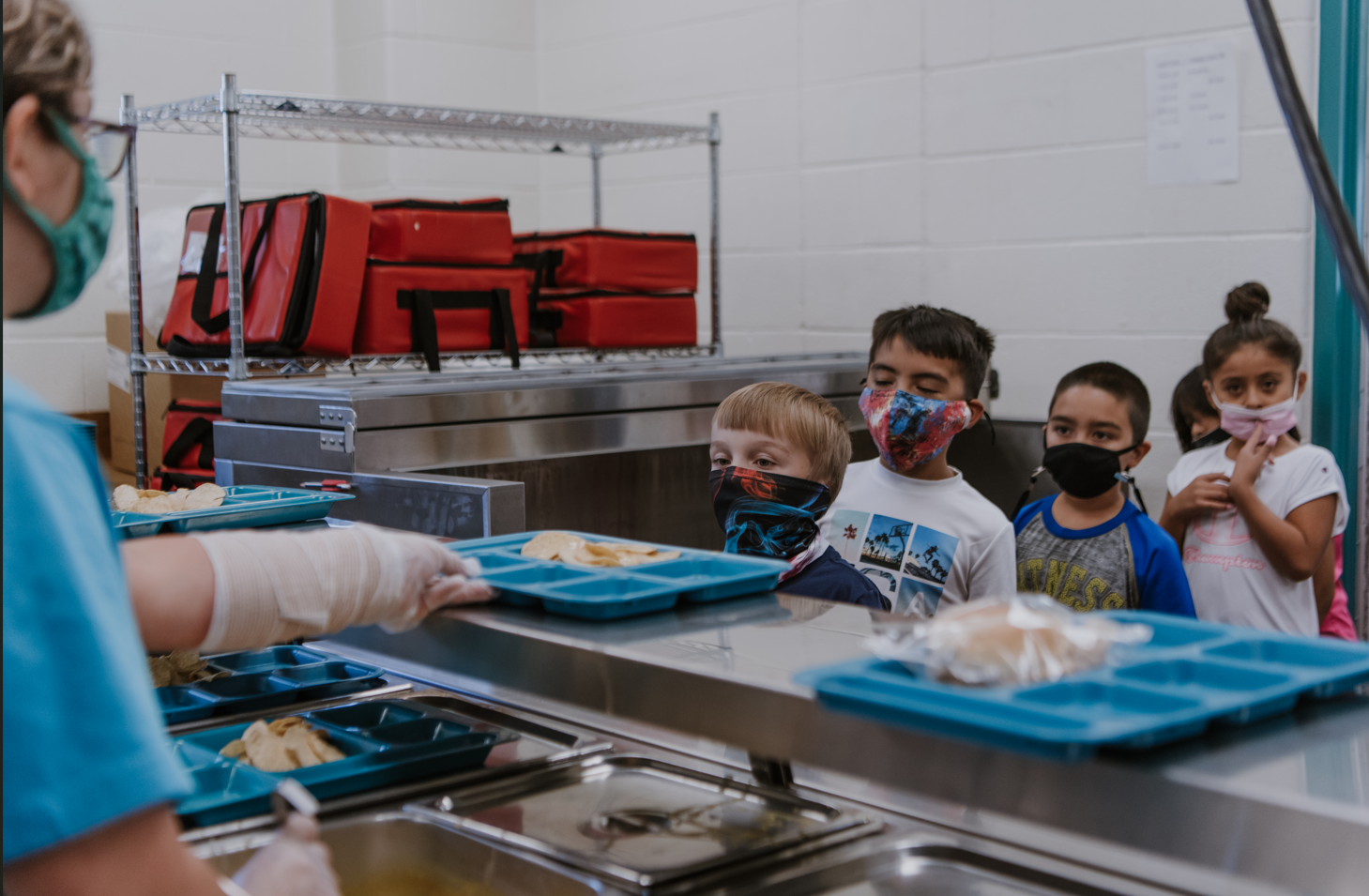 a group of kids wearing face masks and standing in a cafeteria